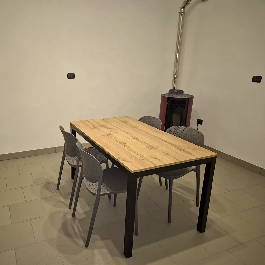 Tavolo solido con top in legno effetto rovere e struttura a ponte in metallo nero.